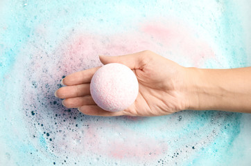 Woman holding color bath bomb over foam, top view