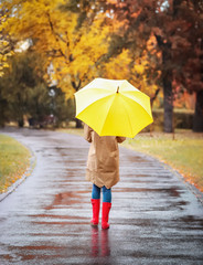 Woman with umbrella taking walk in autumn park on rainy day