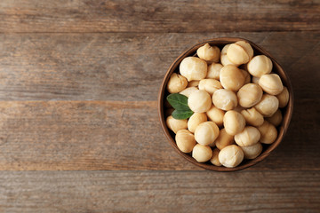 Bowl with shelled organic Macadamia nuts and space for text on wooden background, top view