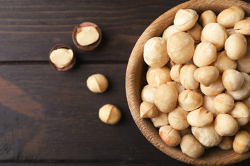Bowl with shelled organic Macadamia nuts and space for text on wooden background, top view