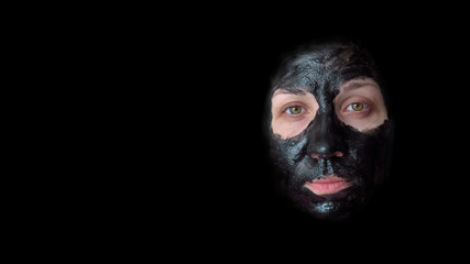 Young woman. Black cosmetic mask on the face. Black background. Close-up portrait. A towel on your head. Wearing a housecoat. Design element.