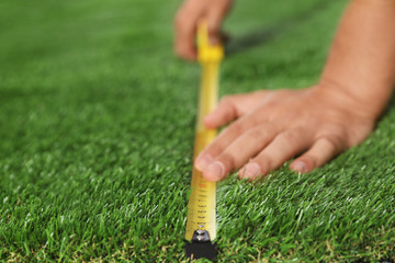 Man measuring artificial grass carpet indoors, closeup