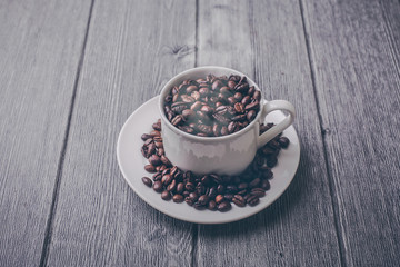 Roasted premium coffee bean in a white cup on black  and wooden background.