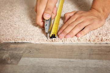 Man cutting new carpet flooring indoors, closeup. Space for text