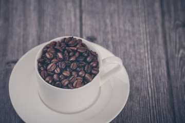 Roasted premium coffee bean in a white cup on black  and wooden background.