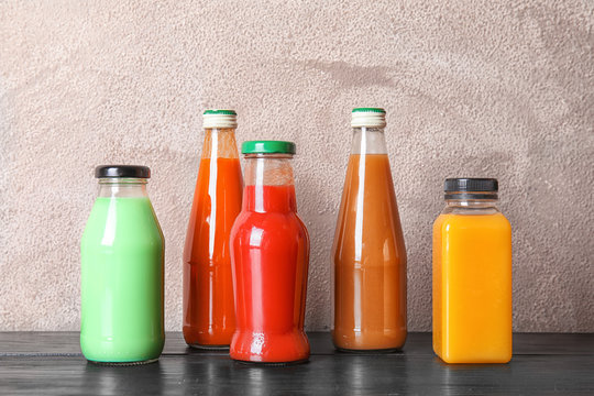 Bottles with different drinks on table against color background