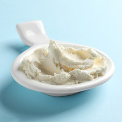 Serving spoon with tasty cream cheese on color background