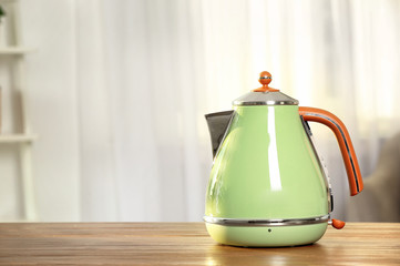 Stylish electrical kettle on table against blurred room interior. Space for text