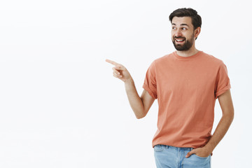 Amused and happy handsome 30s man with beard laughing and smiling, pointing and looking left...