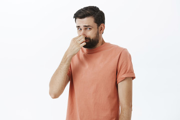 Gosh it stinks. Disgusted and displeased unhappy male with beard closing nose with fingers looking...