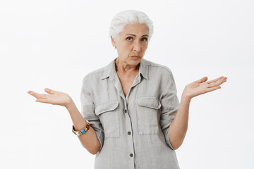 Waist-up shot of clueless unsure cute granny with white hair shrugging with hands spread aside being questioned and unaware what happening trying find answers over gray background