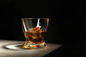 Golden whiskey in glass with ice cubes on table. Space for text