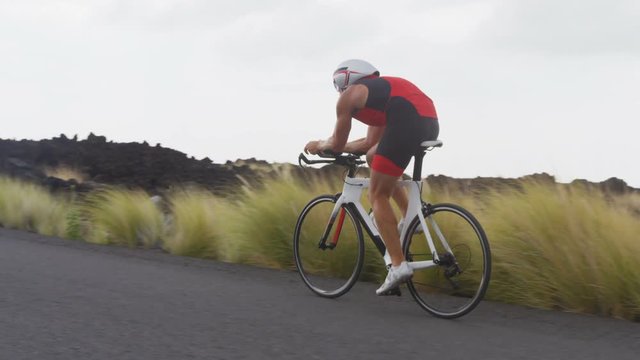 Triathlon man cycling - male triathlete biking on triathlon bike. Cyclist on professional triathlon bicycle wearing time trail helmet for ironman race. SLOW MOTION.
