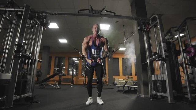 Male bodybuilder training chest muscles exercise using cable cross over machine for body mass. Workout and bodybuilding sport concept. Man in gym doing pulls weight exercise in slow motion.