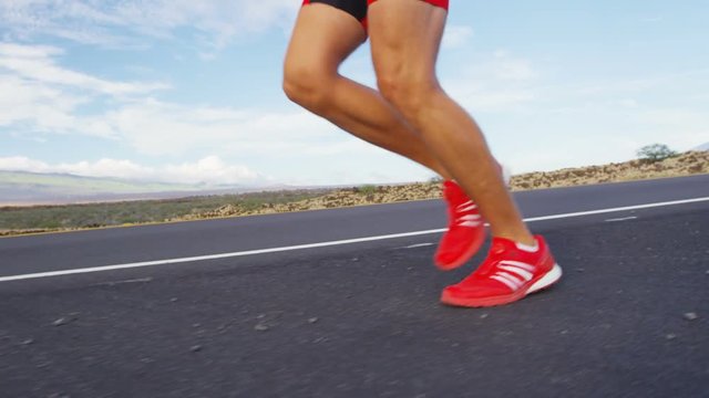 Running shoes on male triathlete runner - close up of feet running on road. Man jogging outside exercising training for triathlon ironman. SLOW MOTION RED EPIC.