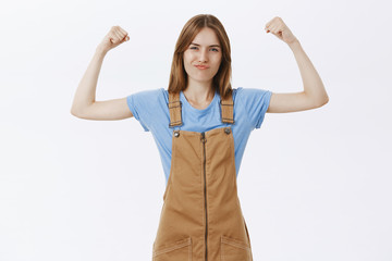 Portrait of proud, confident and strong female femenist in stylish overalls over blue t-shirt...