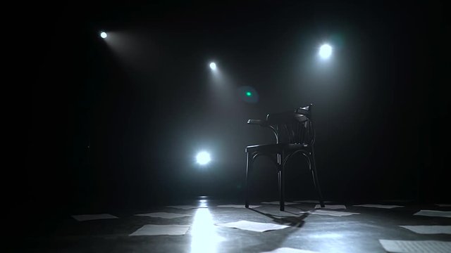 Chair stands in the middle of a dark studio with lanterns on the floor sheets scattered. Black smoke background