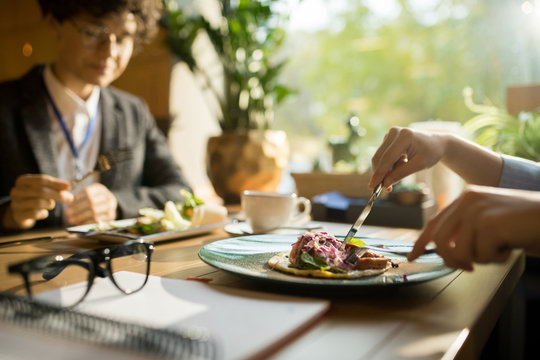 Close-up Of Lady Sitting At Table With Business Partner And Eating Tasty Food In Restaurant, She Cutting Meat With Knife And Fork