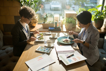 Serious young multiethnic conference participants in smart casual clothing sitting at table and...