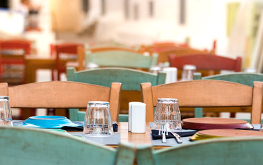 Perspective view of a wooden table with chairs, glasses and plates outdoors in a Greek taverna in Hydra, Greece.