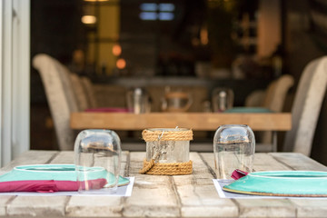 Perspective view of a wooden table with chairs, glasses and plates outdoors in a Greek taverna in Hydra, Greece.