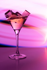 Cocktail glass with a drink and ice cubes in the neon light of a nightclub