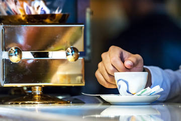 A espresso cup on a marble counter next to a male hand, indoors.