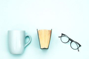 Glasses, cup and book on a light blue background.