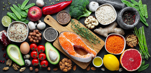Healthy food clean eating selection: fish, fruit, nuts, vegetable, seeds, superfood, cereals, leaf vegetable on black concrete background. Flat lay