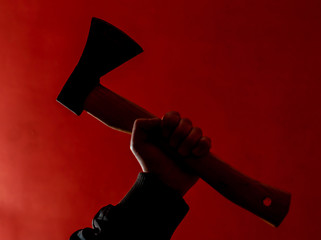 hand holds ax in the dark on red background