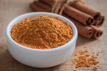 Cinnamon powder and cinnamon sticks on wooden table.