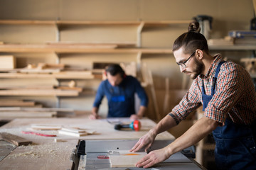 Side view portrait of modern young man working with wood standing at table in  in carpenters workshop, copy space