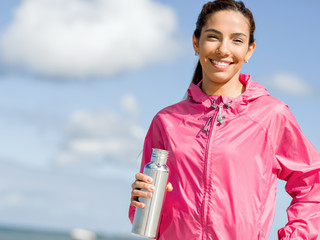 Beautiful girl in sport clothes drinking water after workout on the beach