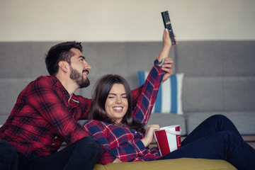 Couple fighting for remote control while watching TV at home