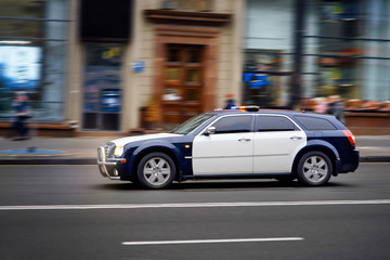 Fototapeta na wymiar Modern police car chases the offender at high speed with the siren and lights in the city. Policemen serve on city roads. Rush to the scene. Prevention of crime. Elite Police Unit.Charged car racing