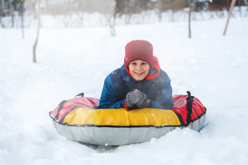 Fototapeta na wymiar Happy teenage boy sliding down hill on snow tube laughing and showing excitement while he slides downhill. Snow tubing on winter day outdoors. Winter activity, leisure and entertainment concept