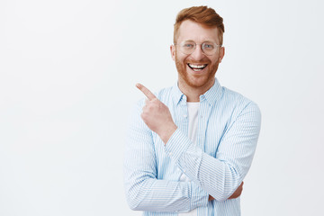 Friendly redhead man with bristle in transparent glasses and striped shirt pointing at upper left...