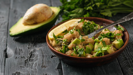Salad of amaranth seeds, avocado, lemon and parsley with olive oil and half avocaco on a rustic table.