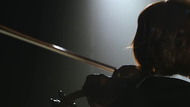 Girls standing back and playing the violins in a dark room. Black smoke background