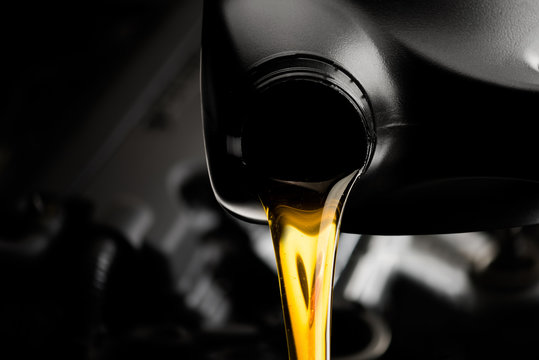 Pouring oil motor car  lubricant  from black bottle on engine background , service oil change auto repair shop