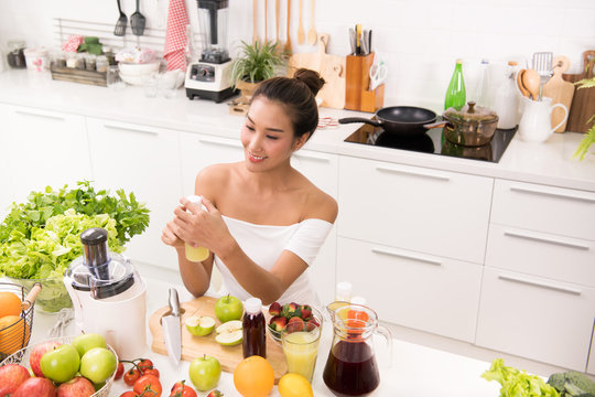 Asian woman in a kitchen with fruits and vegetables and juice
