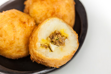 Preparation steps of traditional Colombian dish called stuffed potatoes : Ready stuffed potatoes served in a black ceramic dish isolated on white background