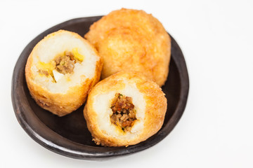 Preparation steps of traditional Colombian dish called stuffed potatoes : Ready stuffed potatoes served in a black ceramic dish isolated on white background