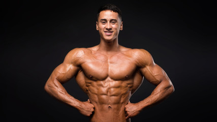 Fototapeta premium Strong smiley fitness model showing muscles over dark background.