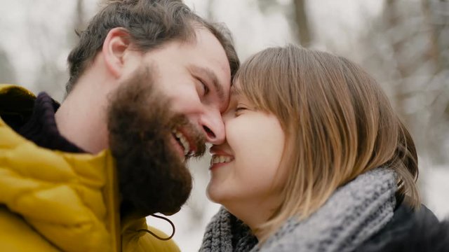 A young guy and a girl dressed in warm winter clothes, enjoy the presence of each other in a snowy winter park. closeup kiss. 4k slow motion.