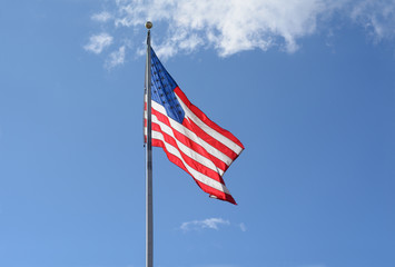 Backlit American flag on flagpole on a windy day against blue sky with light clouds