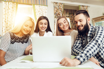 Smiling young friends using laptop in coffee shop