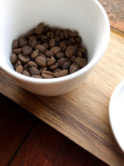 Close up roasted coffee beans in a white ceramic cup on wooden tray in natural light 