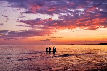 Silhouette of people playing in to the sea with dramatic sunset sky
