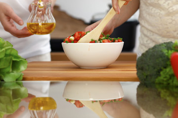 Closeup of human hands cooking in kitchen. Mother and daughter or two female friends cutting vegetables for fresh salad. Friendship, family dinner and lifestyle concepts